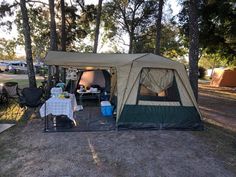 a tent set up in the middle of a park with picnic tables and chairs next to it