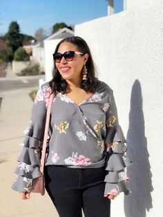 a woman standing next to a white wall wearing black pants and a gray top with flowers on it