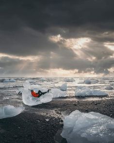 a person is laying on an iceberg in the middle of the ocean under a cloudy sky