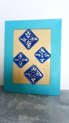 four blue and white tiles in a wooden frame on the floor with a wall behind them