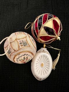 three decorative ornaments are sitting on a black cloth surface, one is white and the other is red