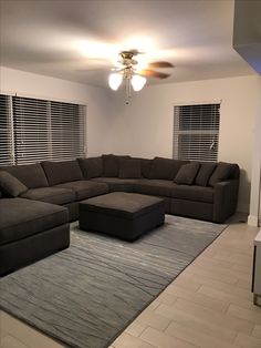 a living room with a large sectional couch and ottoman in the middle of the room