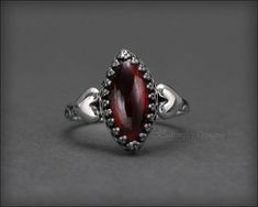 This gorgeous ring is uniquely beautiful and has a wonderful Victorian feel! A perfect gift for your sweetheart. The gemstone of your choice is set a gallery, bezel setting with two sterling silver hearts hugging each side. The ring has been oxidized to bring out all the lovely details. 𝙏𝙝𝙞𝙨 𝙙𝙚𝙨𝙞𝙜𝙣 𝙞𝙨 𝙤𝙧𝙞𝙜𝙞𝙣𝙖𝙡 𝙩𝙤 𝙇𝙀 𝙅𝙚𝙬𝙚𝙡𝙧𝙮 𝘿𝙚𝙨𝙞𝙜𝙣𝙨® 𝙃𝙖𝙣𝙙𝙘𝙧𝙖𝙛𝙩𝙚𝙙 𝙗𝙮 𝙇𝙖𝙪𝙧𝙚𝙣 𝙀𝙡𝙞𝙯𝙖𝙗𝙚𝙩𝙝. 𝙈𝙖𝙙𝙚 𝙞𝙣 𝙩𝙝𝙚 𝙐𝙎𝘼. • sold individually• made-to-order• s Silver Marquise Birthstone Ring As A Gift, Silver Marquise Birthstone Ring For Gift, Marquise Sterling Silver Jewelry Gift, Sterling Silver Marquise Jewelry Gift, Sterling Silver Marquise Jewelry For Gifts, Marquise Jewelry With Gemstone Accents As Gift, Marquise Sterling Silver Promise Rings, Sterling Silver Marquise Jewelry For Anniversary, Wedding Garnet Cabochon Jewelry