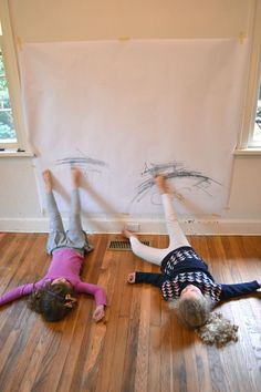 two children are laying on the floor with their hands in the air and one child is upside down