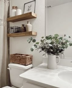 a white toilet sitting next to a bathroom sink under a wooden shelf filled with flowers