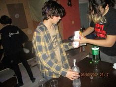 two young people standing at a table with drinks in front of them and one person holding a bottle