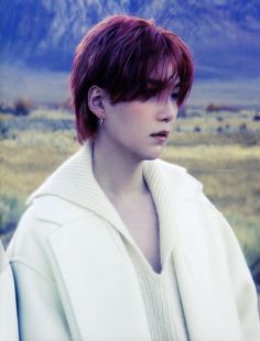 a woman with red hair wearing a white coat and looking off to the side in an open field