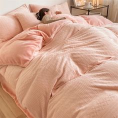 a woman laying in bed with pink comforter and pillows