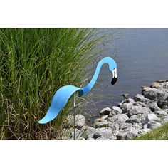 a blue flamingo sculpture sitting next to a body of water