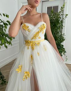 Details:-White tulle fabric with embroidered illuminated golden petals -Bustier top with straps-Heart shaped with fitting boning-Draped Wrap Top-A-line silhouette-Leg slit-Floor-length-Wide long gathered skirt -Side pockets- Decorative y... Prom Dress White, Lace Long Prom Dress, Teuta Matoshi, Special Occasion Gowns, Floral Prom Dresses, White Evening Dress, Floor Length Prom Dresses, Ribbon Belt, Yellow Ribbon