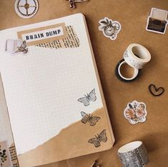 an open notebook with stickers on it next to some coffee cups and other items