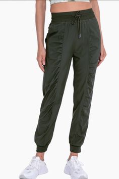 These flattering lightweight woven olive joggers are ideal for any indoor or outdoor adventure! Enjoy the convenient adjustable drawstring waist, ribbed hem and waistband, ruched front detailing, roomy side pockets, and a ribbed rear yoke for max mobility and comfort.Shell: 94% polyester 6% spandexRib: 100% polyester27" inseamColor- Olive Green Green Nylon Parachute Pants Athleisure, Green Nylon Parachute Pants For Athleisure, Spring Utility Joggers With Elastic Waistband, Sporty Green Joggers For Outdoor Activities, Functional Drawstring Bottoms For Spring, Green Athleisure Sweatpants For Outdoor, Spring Functional Drawstring Bottoms, Green Drawstring Bottoms For Outdoor Activities, Stretch Green Joggers With Elastic Waistband