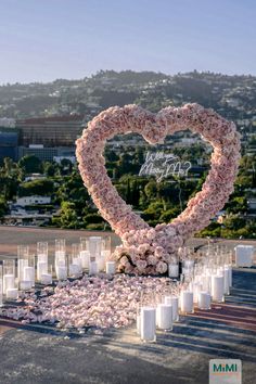 a heart - shaped arrangement of flowers and candles sits in the middle of a parking lot