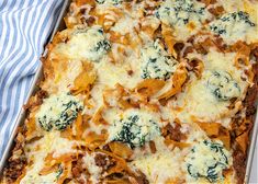 a casserole dish with cheese, meat and spinach in it on a towel