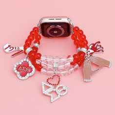 an apple watch with red bracelets and charms on it's wrist, against a pink background