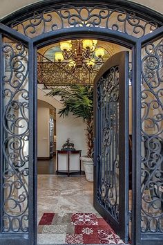 an ornate iron door is open to reveal the entryway and foyer area with chandelier