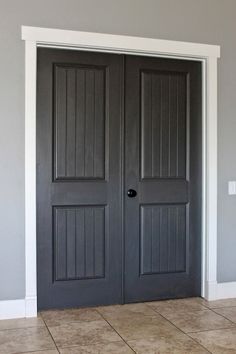 an empty room with two black doors and tile flooring on one side, the door is painted dark gray