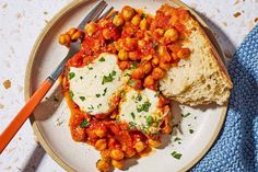 a white plate topped with meat covered in sauce and chickpeas next to bread