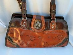 This shoulderbag is a caramel color on the bottom half with a brown color top, sides and bottom of bag. The strap drop is 12.5".  They are brown on one side and caramel on the other side.  There are etched silver hardware holding them on to bag. A zipper closes the purse and there is also a flap with a snap closure. The inside has a satiny lining with 3 compartments. 1 is open with 2 slip pockets 1 is zipped 1 is open with a zipped pocket There are shamrocks imprinted in the outside fa Mcm Logo, Caramel Color, Michael Kors Hamilton, Cute Jewelry, Silver Hardware, Brown Color, Snap Closure, Bags Handbags, Top Handle Bag