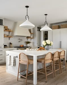 a kitchen with two pendant lights over the island and four stools in front of it