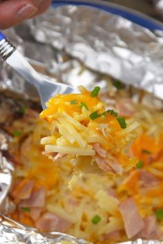 a person holding a fork full of food in foil wrapper with meat and cheese on it