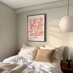 a bed with white sheets and pillows in a bedroom next to a wall hanging above it