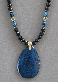 NOTE: Fire Agates are natural volcanic stone and they are not perfect due to the nature of the stone. However, they are very pretty! The pendant is unusual and it is thicker than most because it comes from volcanic rock. This is a lovely teardrop shaped Black and Blue Fire Agate Pendant Necklace.   The beads in the necklace are genuine black agate with blue crystal beads that pick up the colors of the pendant with silver crystal accents.   The pendant is polished. The pendant measures 2 inches long x 1 1/2 inches wide.  This is a unique one of a kind necklace.  It's 16 inches long and adjustable to 20.  All my jewelry is unique and one of a kind. Similar quality jewelry is priced at double. I source the stone pendants from all over the world. All pendants and necklaces are made with semipr Jewellery Patterns, Wooden Bead Jewelry, Jewelry 2024, Blue Crystal Beads, Beaded Designs, Fall Fashions, Agate Pendant Necklace, Dragon Vein Agate, Volcanic Stone