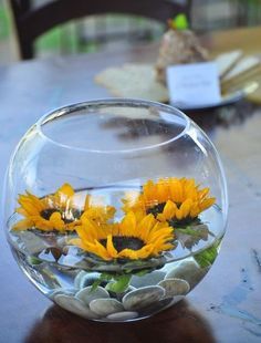 sunflowers and rocks in a glass bowl on a table