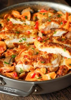 a pan filled with chicken and vegetables on top of a wooden table