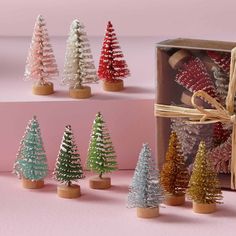 several small christmas trees are in a wooden box and tied with twine, on a pink background