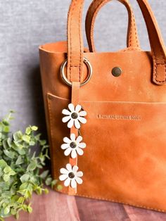 a brown leather bag with white flowers on the front and side, sitting next to a green plant