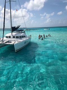 people are swimming in the ocean near a boat that is floating on clear blue water