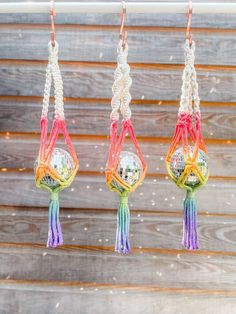 three colorful macrament balls hanging from hooks on a wooden fence with lights in the background