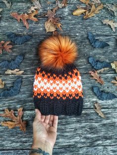 a person is holding their hand up to a hat with an orange pom - pom