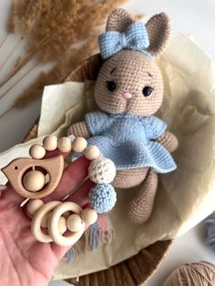 a hand is holding a crocheted teddy bear with a blue dress on it