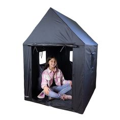 a woman sitting inside of a black tent on top of a white floor next to a wall