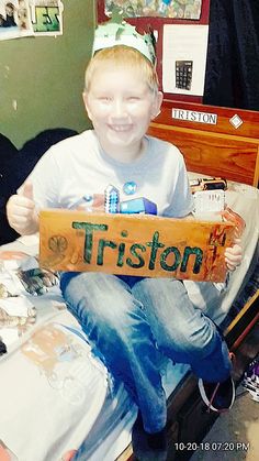 a young boy sitting on top of a bed holding a sign that says tristor