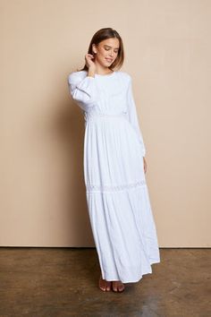 a woman standing in front of a wall wearing a white dress