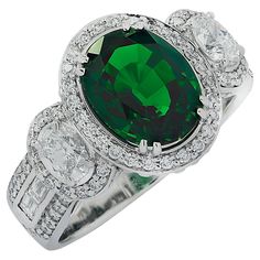 Spectacular Vivid Diamonds ring crafted in 18 karat white gold showcasing a stunning rich green oval cut Tsavorite weighing 3.38 carats, accented by two round oval cut diamonds weighing approximately .40 carats total, G color, VS clarity, and 84 round brilliant and baguette cut diamonds weighing approximately 1 carat total, F-G color VS clarity. The Tsavorite is surrounded by a diamond halo, and is flanked by two oval cut diamonds laced with round brilliant cut diamonds. The shank is adorned wit Ornate Ring, Colored Stone Rings, Green Oval, Diamonds Ring, Expensive Jewelry, Rich Green, Baguette Cut Diamond, Ring Crafts, Oval Cut Diamond