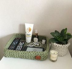 a white table topped with a green basket filled with cosmetics and other items next to a potted plant