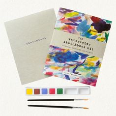 the watercolor sketch book is next to some paintbrushes and an artist's palette