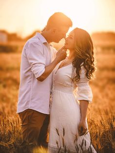 a man and woman standing next to each other in a field with the sun behind them