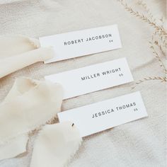 three tags with names on them are laying on a bed sheet that is unmade