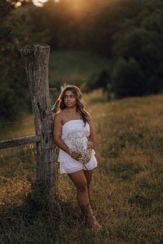 a woman in a white dress leaning against a fence