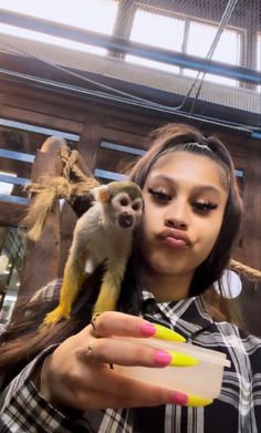 a woman holding a small monkey on her arm and looking at it's face