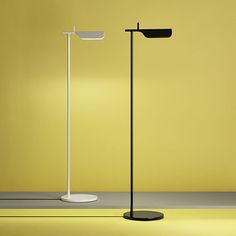 two floor lamps are standing next to each other in an empty room with yellow walls