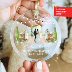 a person holding up a glass ornament with a wedding photo on the front