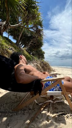 a man laying on top of a beach chair next to the ocean and palm trees