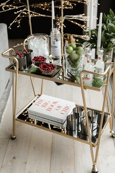 a bar cart with drinks, candles and other holiday decorations on the table in front of a christmas tree