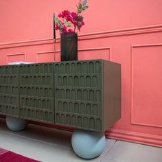 a vase with flowers sitting on top of a cabinet next to a pink wall and rug